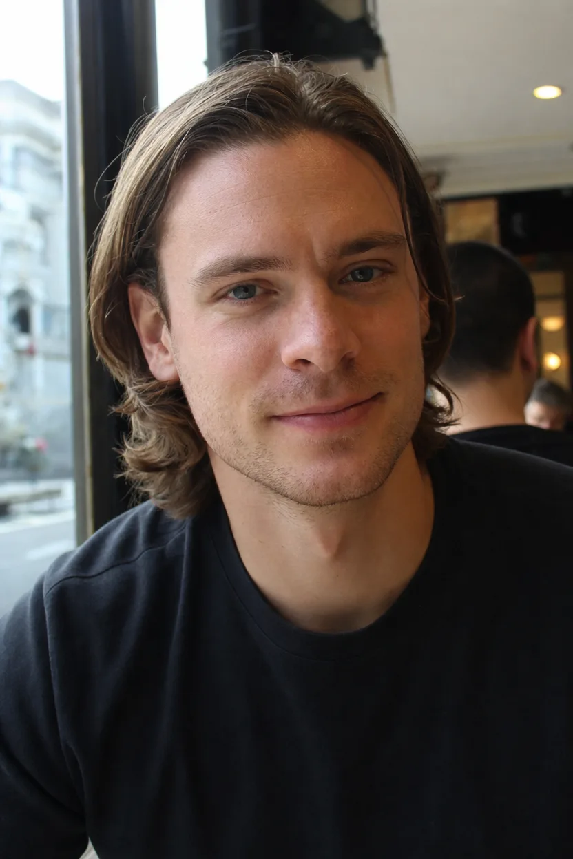 A man with light brown chin-length hair pushed behind his ears, sitting by a cafe window
