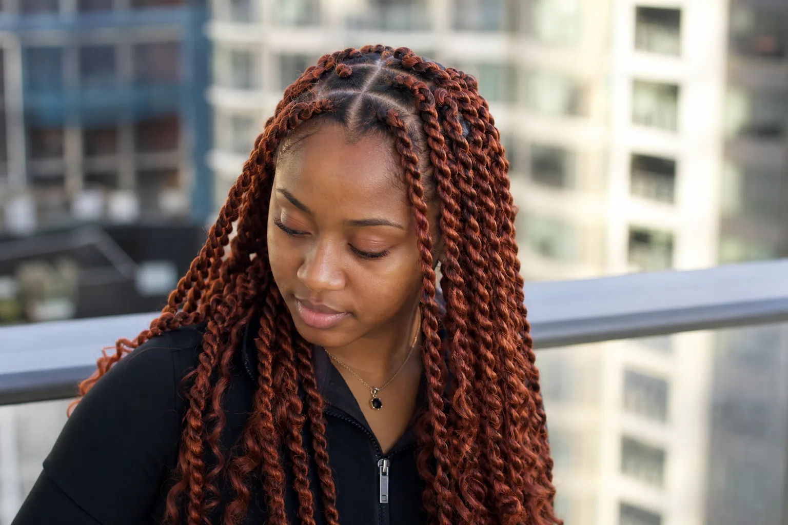 A woman on a balcony with long copper auburn passion twists falling past her chest, wavy loose ends and clean square partings across the crown