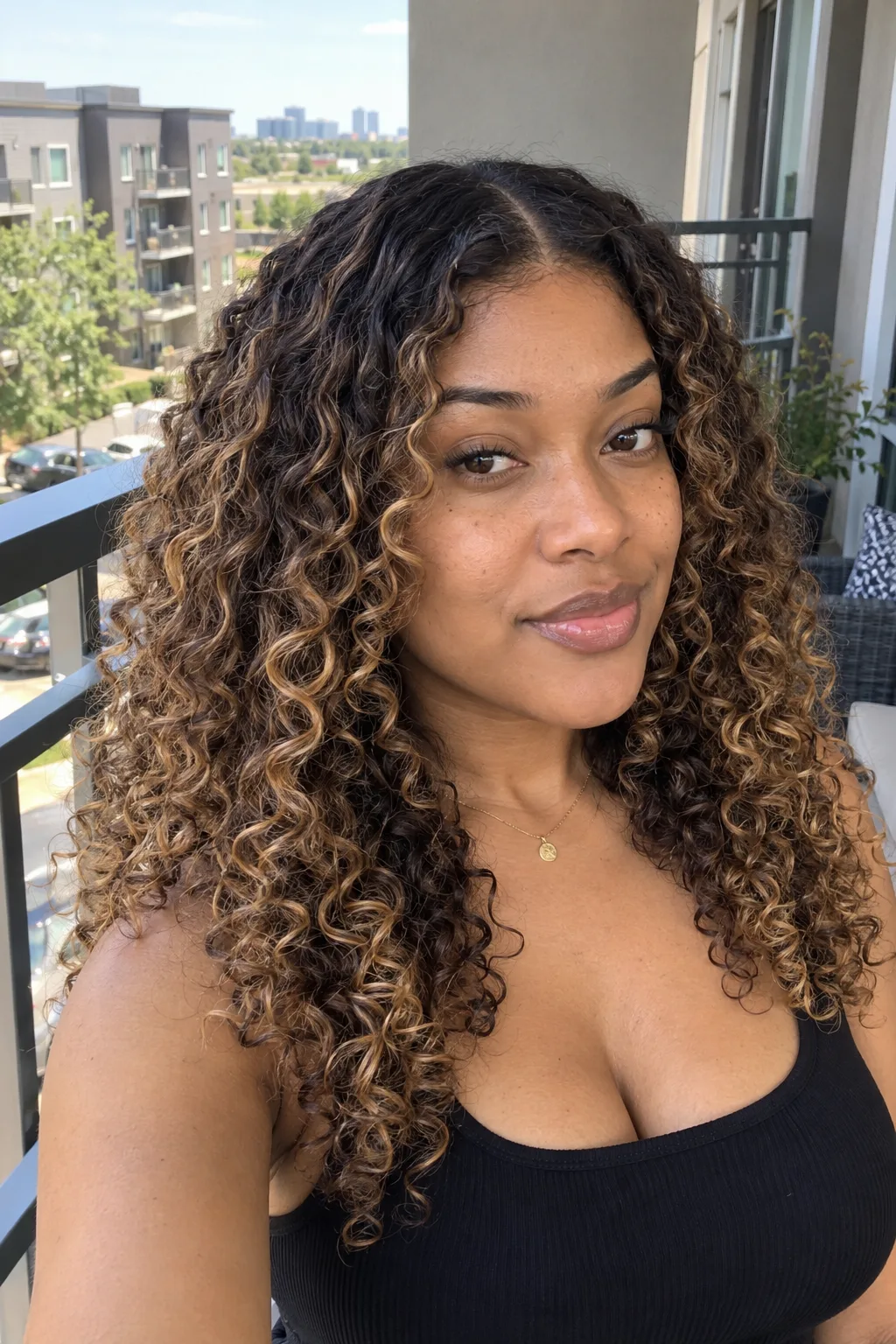 A woman on an apartment balcony with long dark brown curls and honey golden highlights spiraling through them