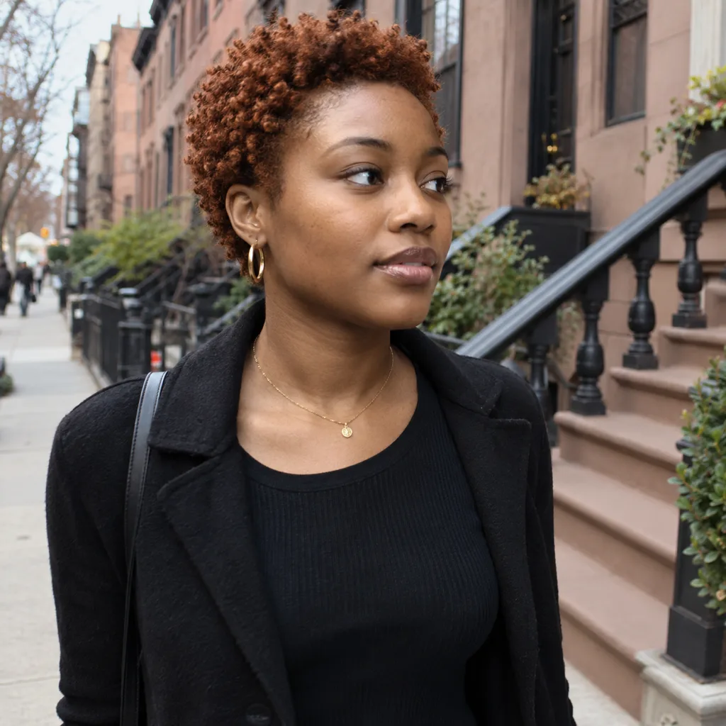 A young woman on a brownstone street with a short copper 4a tapered cut, coils on top and closer at the sides