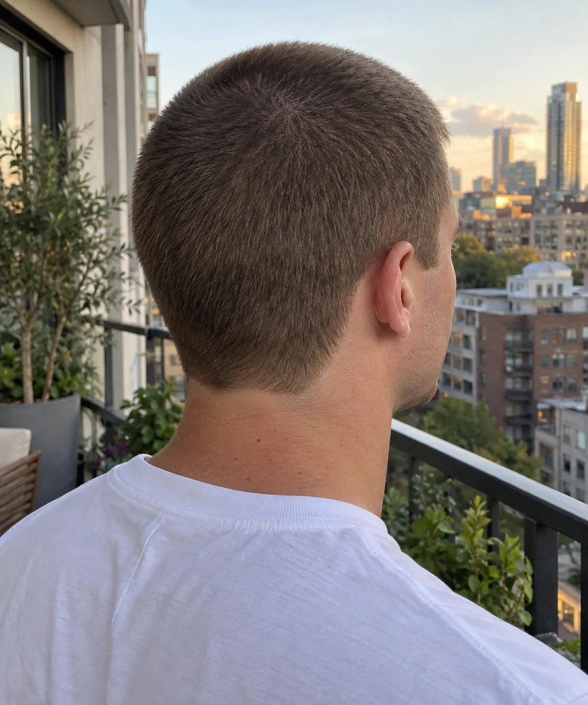 Back of a man's head with an even quarter inch buzz cut and a tidy rounded neckline above a white t-shirt collar