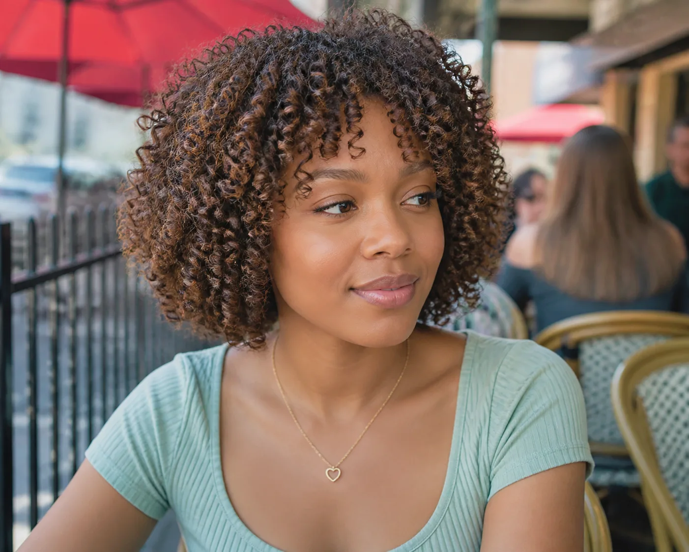 Chin-length curly bob in dark brown with caramel highlights and a curly fringe, at an outdoor cafe
