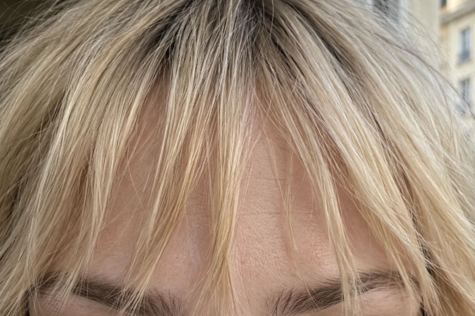 Close crop of a blonde woman's forehead showing point-cut bangs separating into pieces with gaps of skin visible between them