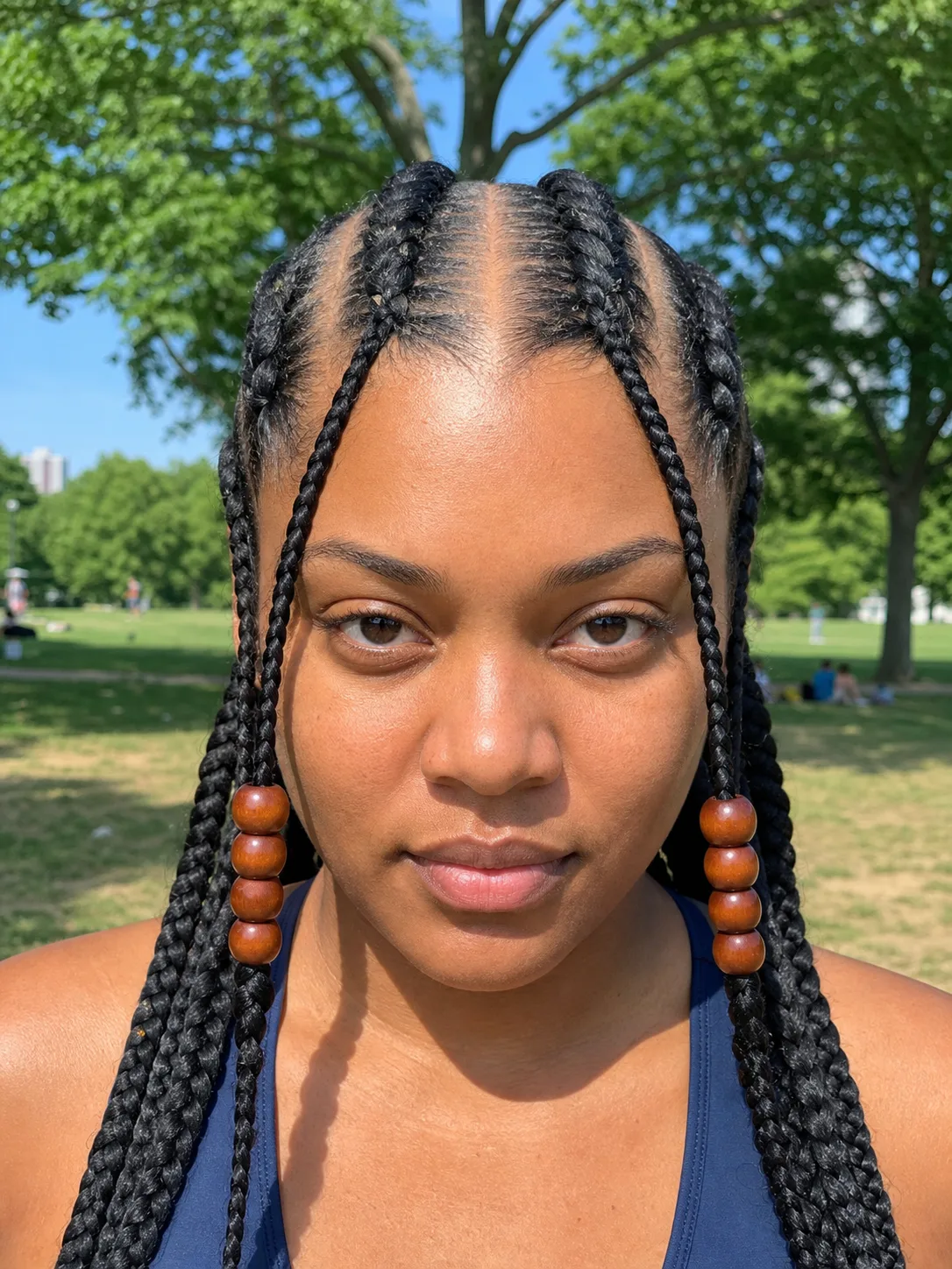 Close portrait with four bold cornrows, a center part, thick beaded side braids, and chunky long braids
