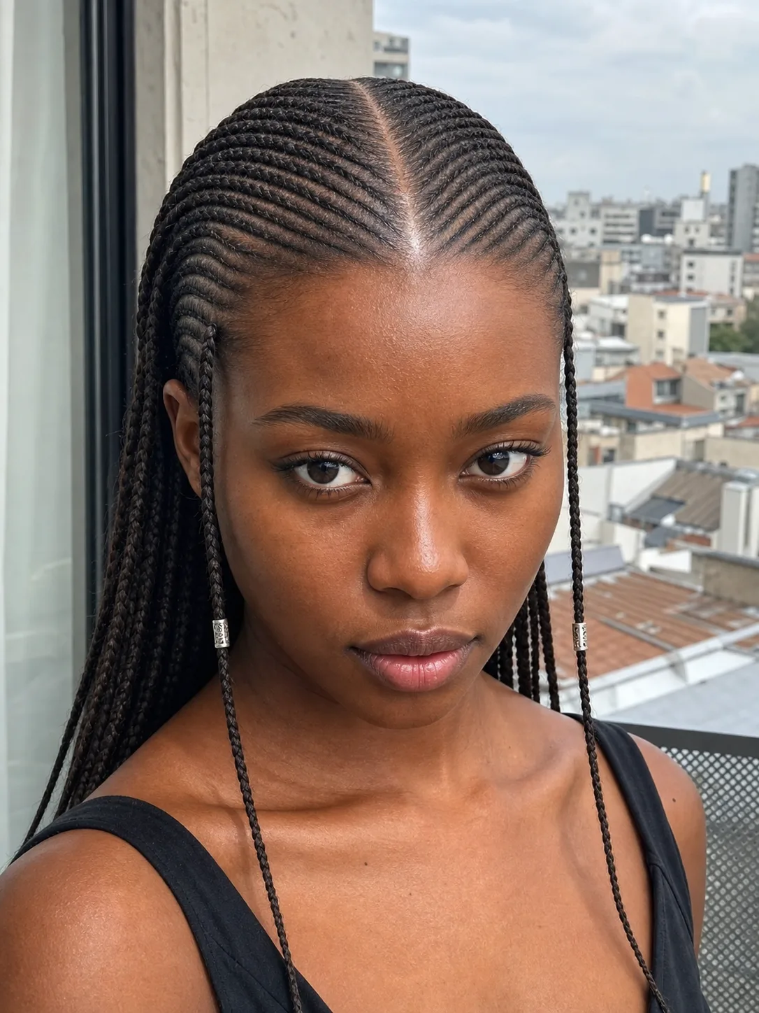 Close portrait with many fine front cornrows, a center part, slim side braids, and long fine braids