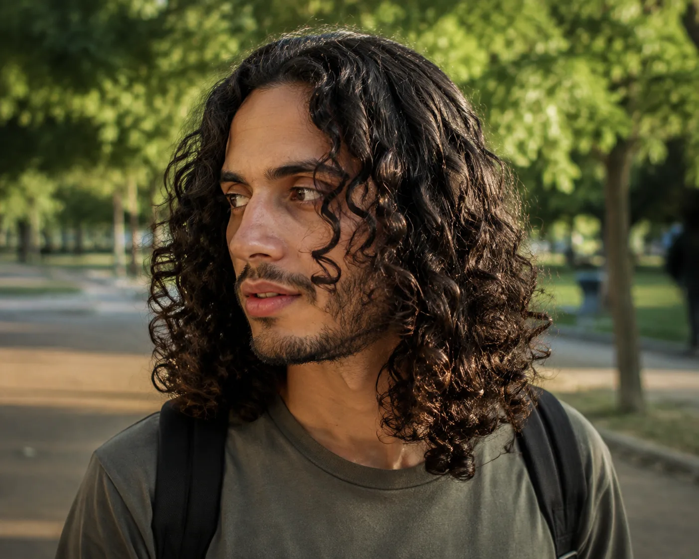 Man walking in a park with shoulder-length brown curls and no shaved sides