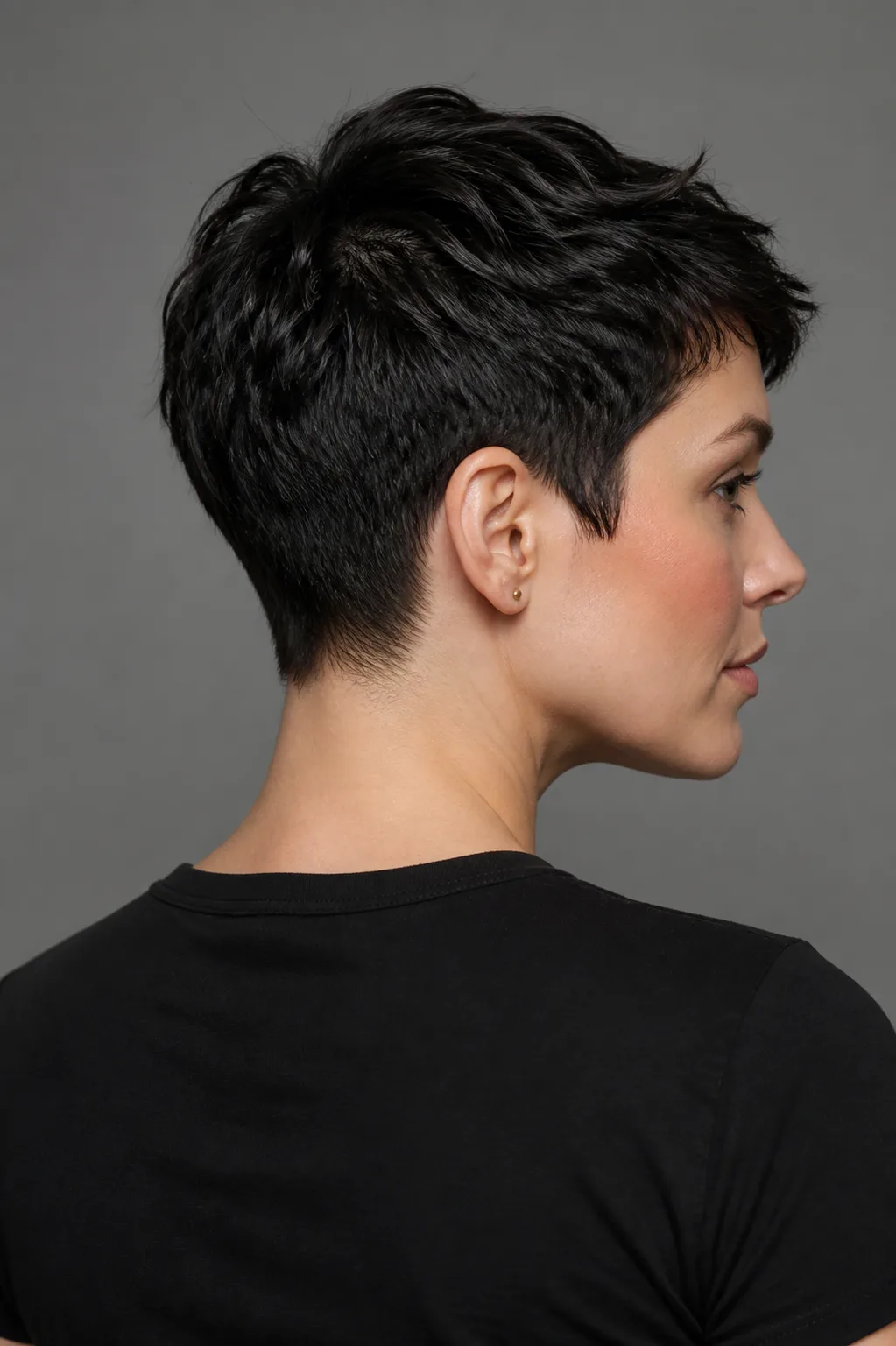 Rear three-quarter view of a woman with a short black pixie crop and softly tapered neckline