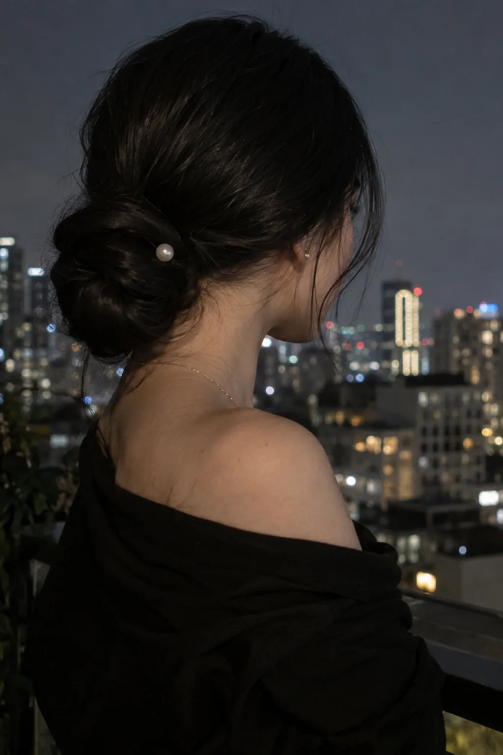 Three-quarter rear view of a woman with very long jet black hair in a smooth low chignon at the nape with a pearl pin