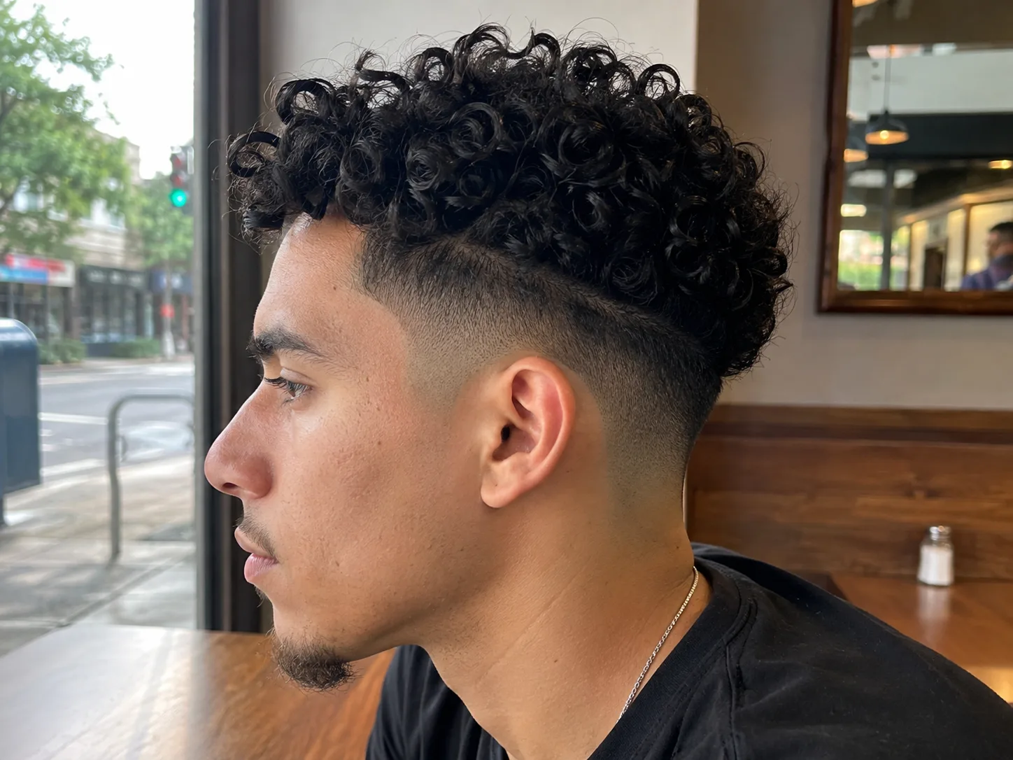 Side profile of a man at a cafe window with the sides faded tight to the skin and a thick bank of curls on top