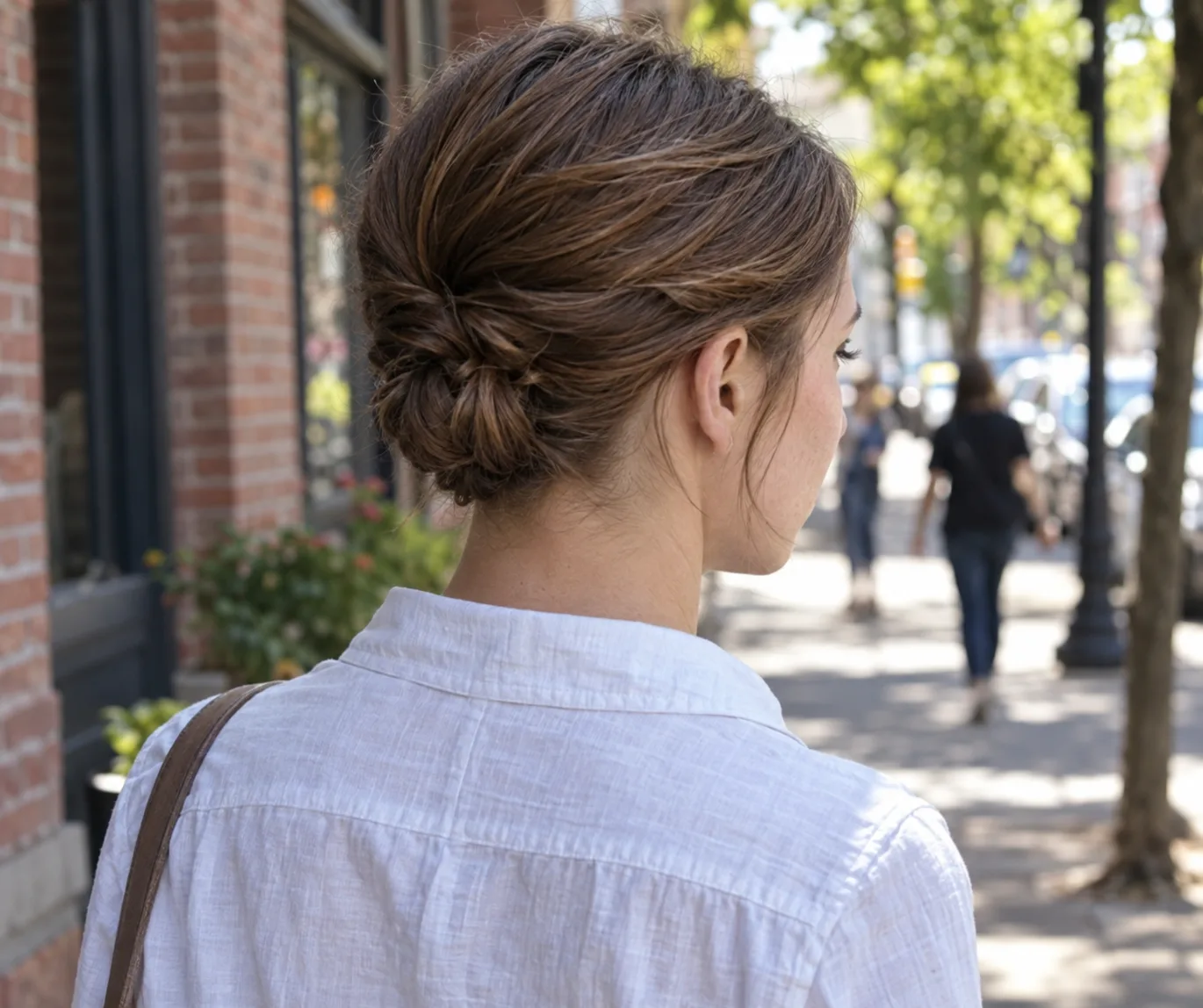 Woman on a city sidewalk with brown hair twisted back into a small low knot at the nape