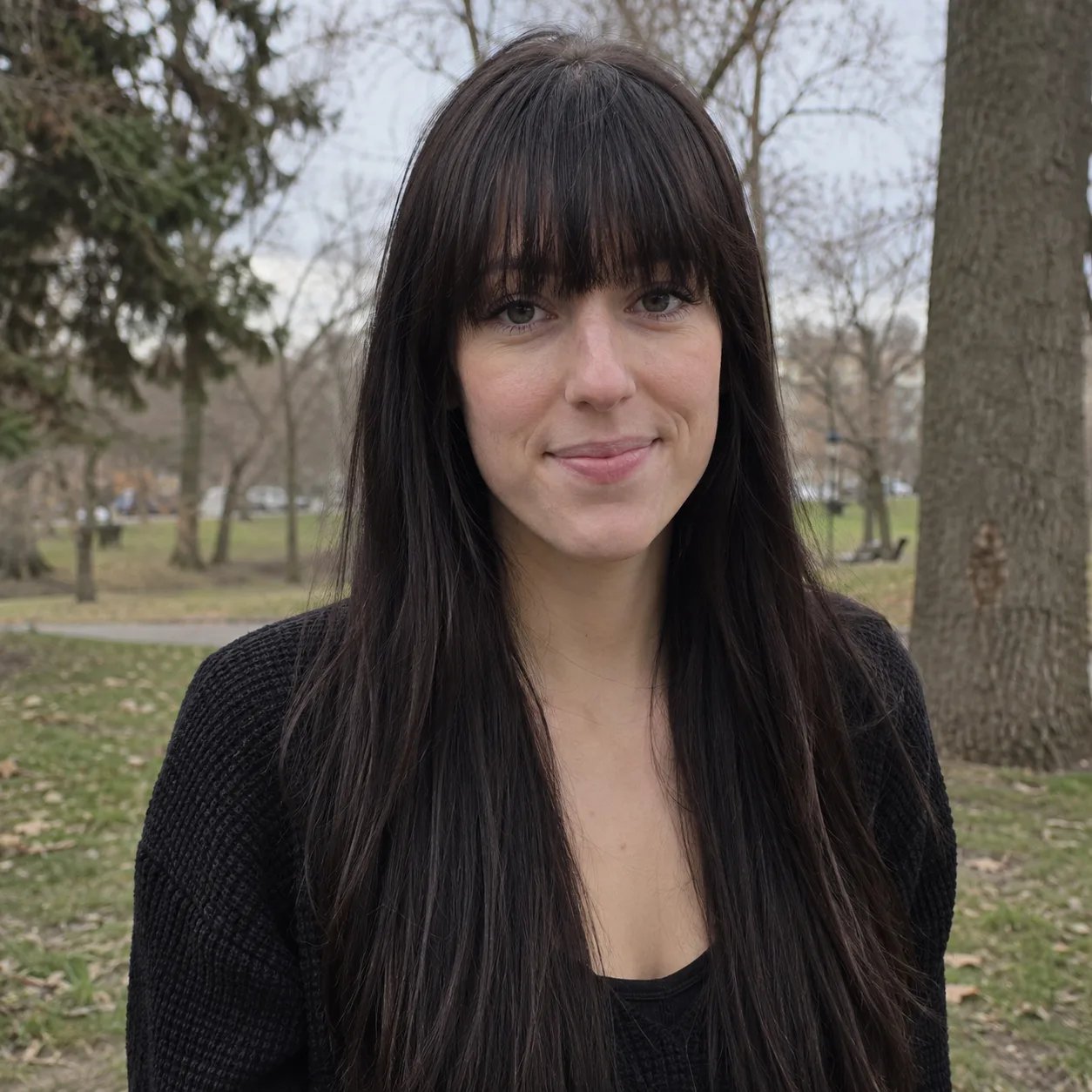 Woman with a long face and long straight black hair in a park, full dense bangs reaching her lashes