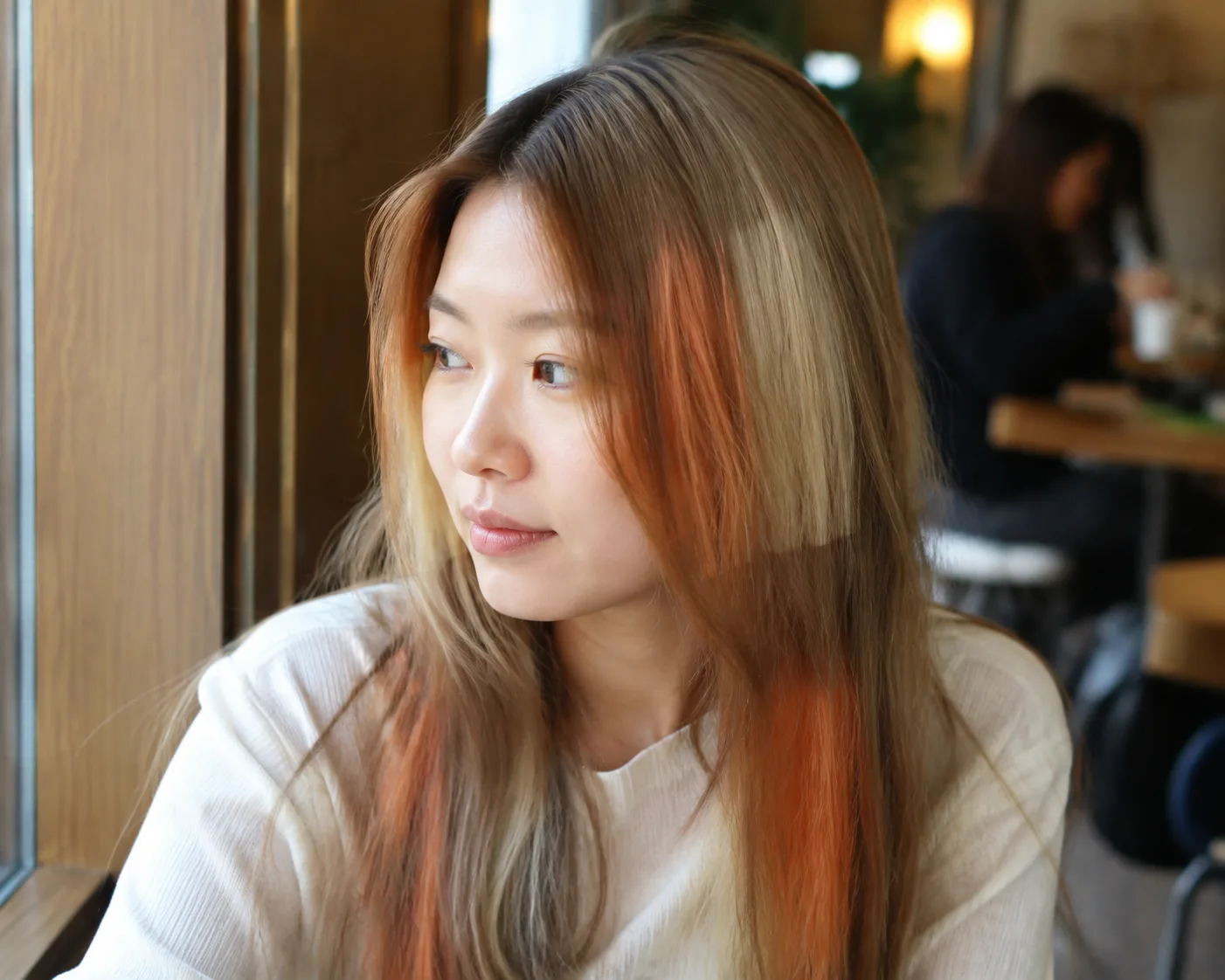 Woman with long straight light brown hair by a cafe window, one copper panel at the front and a pale blonde block at mid length
