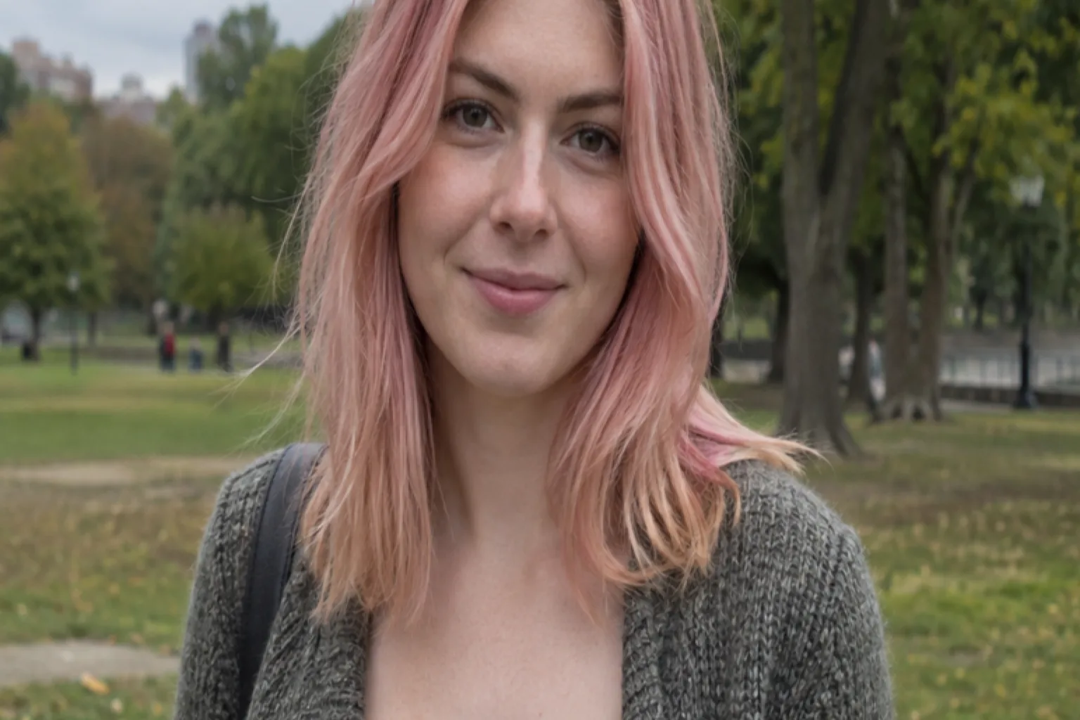 Woman with soft pastel pink shoulder-length hair standing in a park on an overcast day