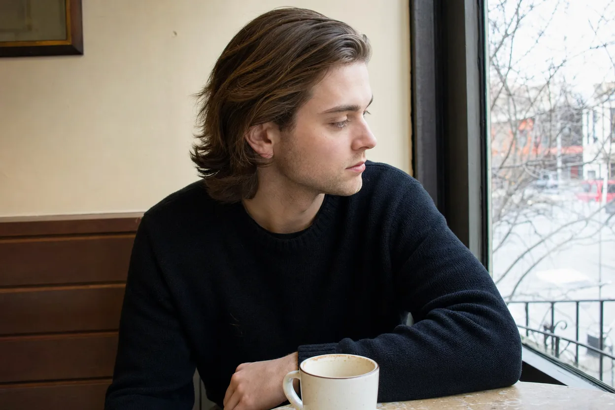 Young man at a cafe window with chestnut hair grown to the jaw all over and swept back from his forehead