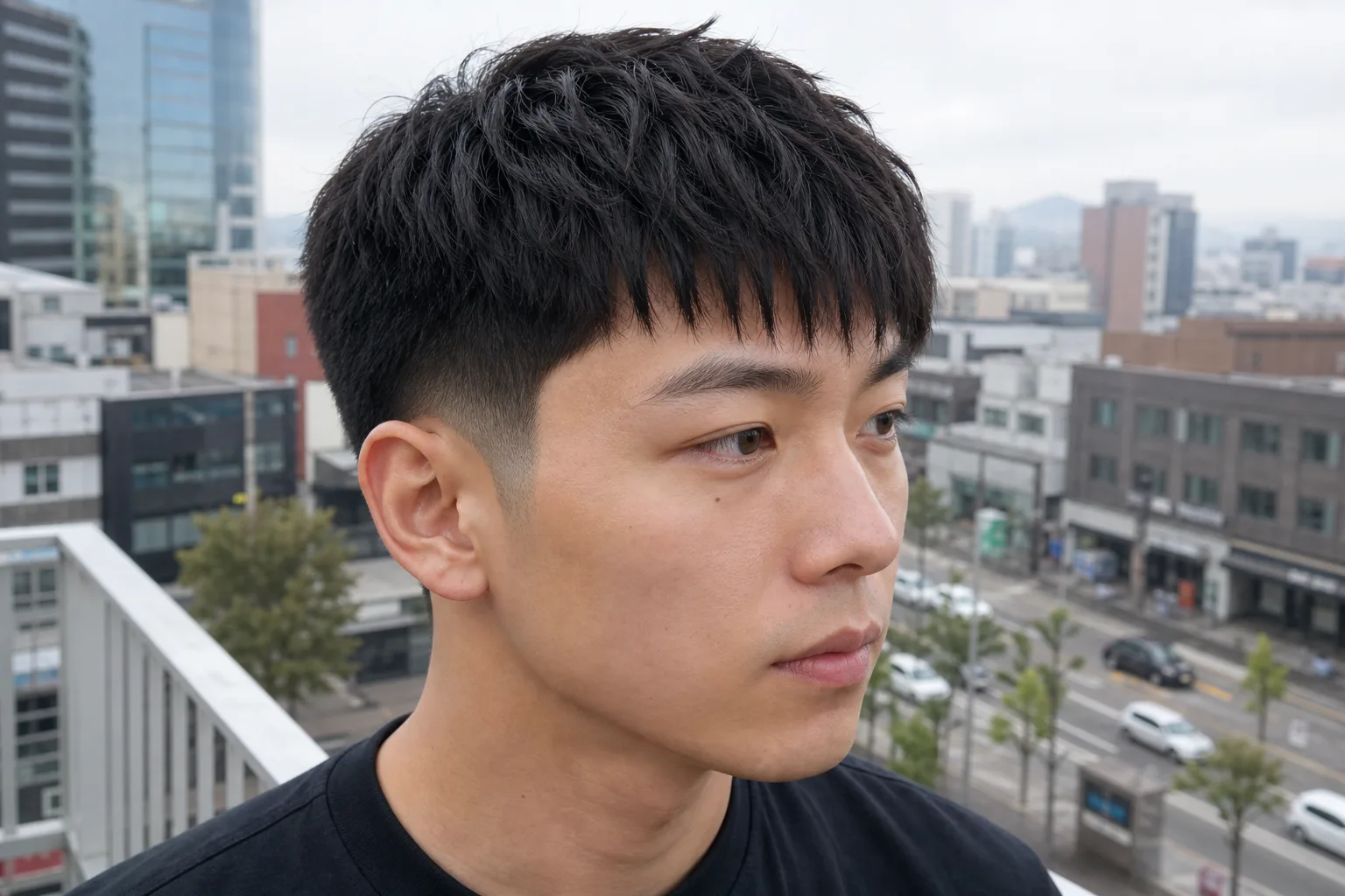 Young man with a low taper fade at the sides and a forward textured fringe on top, three quarter view on a balcony